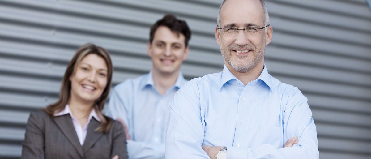 Unternehmer steht vorne mit verschränkten Armen, dahinter ein Mann und eine Frau, beide mit verschränkten Armen. 20-30, 40-50, angestellte, arbeit, arbeiten, arbeitsplatz, arme verschränkt, ausbildung, beruf, bildung, business, büro, chef, dienstleistung, entwicklung, erfahrung, erfolg, erfolgreich, fortbildung, gemeinschaft, gruppe, handwerk, industrie, job, jobsuche, jung, karriere, kaufmann, kollegen, lachen, lernen, leute, lächeln, menschen, mitarbeiter, motiviert, nachfolge, personal, seriös, team, teamwork, unternehmen, vision, wachstum, weiterbildung, ziel, zukunft, zusammen