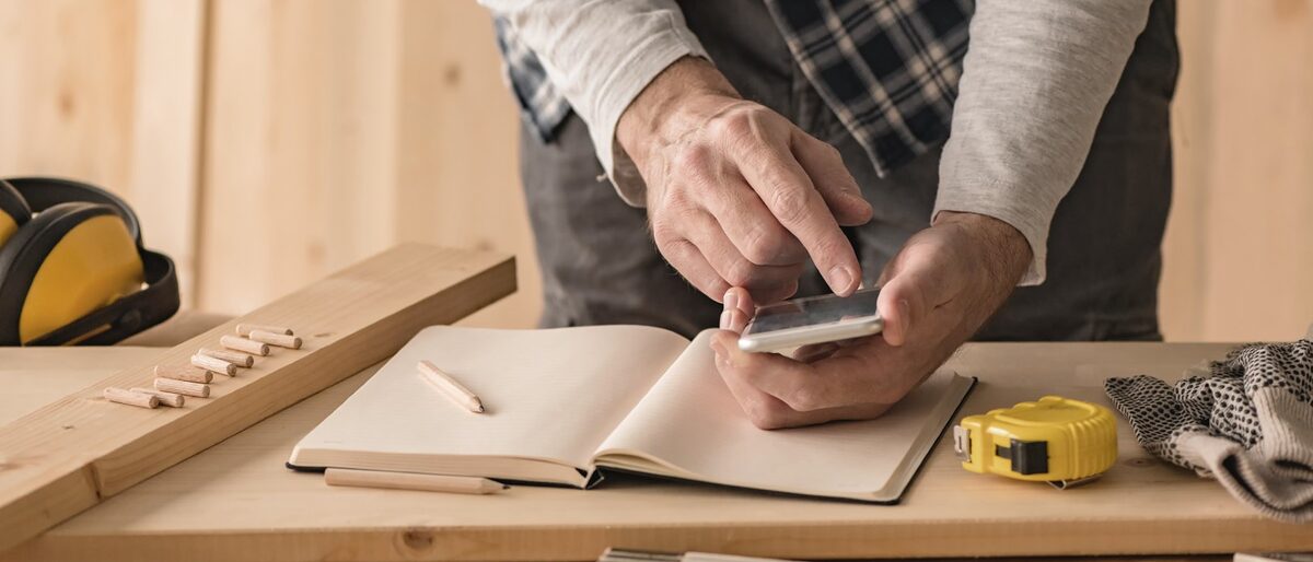 Schreiner bei der Planung eines Projektes, tippt mit dem Finger auf sein Smartphone. Um ihn herum liegen Werkzeuge verteilt auf einem Tisch. Carpenter making project calculation using smartphone app in small business woodwork workshop Schlagwort(e): adult, analyzing, app, application, authentic, calculate, calculation, calculator, carpenter, carpentry, caucasian, contemporary, cost, craft, craftsman, device, diy, equipment, finance, financial, hobby, internet, investment, invoice, male, man, mobile phone, modern, occupation, online, price, professional, project, real people, repair, research, service, small business, smartphone, technology, telephone, tool, trade, using phone, woodwork, work, workplace, workshop