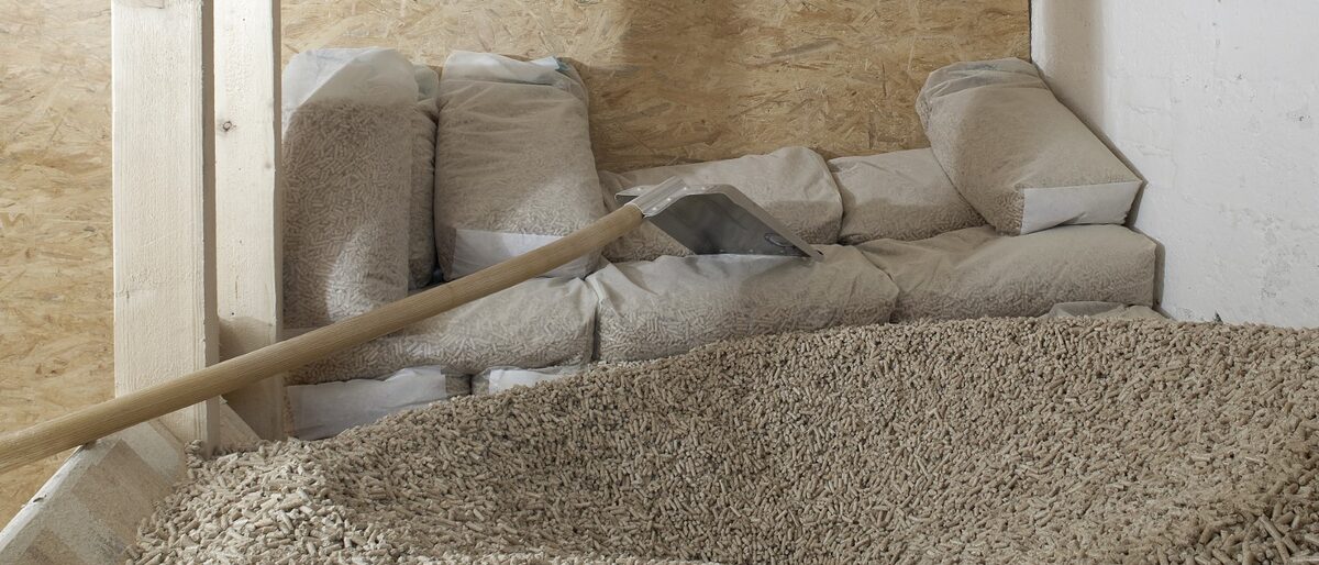 Vorne ein großer Haufen Holzpellets, dahinter eine Schaufel und abgepackte Beutel mit Holzpellets als Inhalt. holzpellets; lager; lagerung; klimaerwärmung; raum; nachhaltig; pelletheizung; heizen; co2; energieträger; holz; pellets; pelletlager; pelletlageraum; heizung; heizanlage; energie; energieversorgung; erneuerbare; energien; bio; wald; biowärme; keller; holzenergie; klima; nachwachsend; regenerativ; umwelt; umweltneutral; wärme; biologisch;