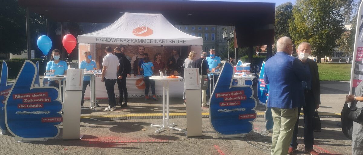 Zelt auf dem Friedrichsplatz in Karlsruhe. Berater-Team im Gespräch mit Besuchern. Titelbild Nachvermittlungsaktion