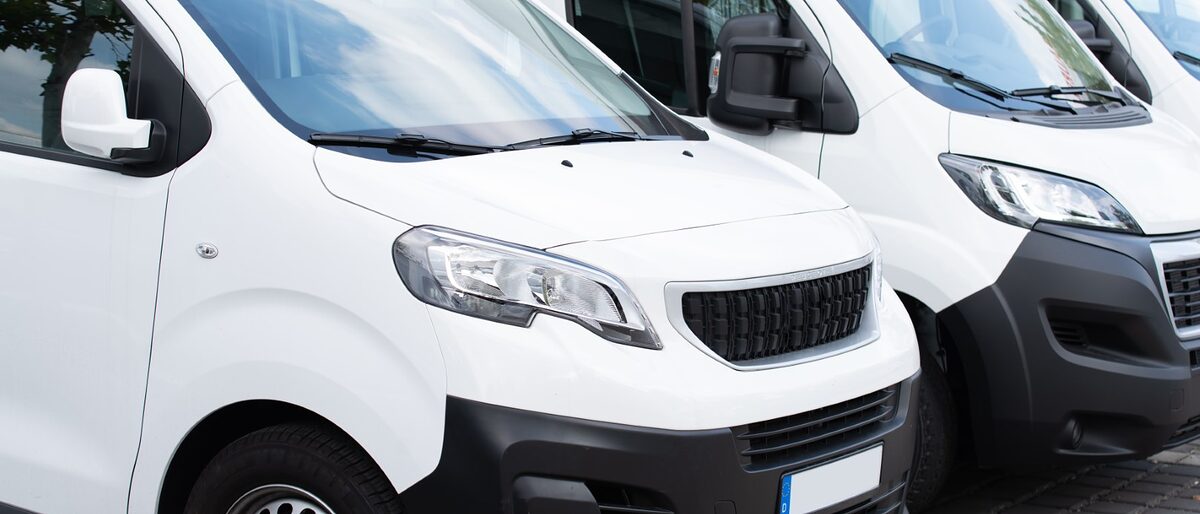 Weiße Nutzfahrzeuge stehen in einer Reihe versetzt nebeneinander. nutzfahrzeuge, transporter, logistik, spedition, transportieren, kleintransporter, weiß, personen, güter, leasing, firma, unternehmen, fahrzeug, nutzen, zuladung, last, überladen, fahrzeugklasse, bus, kleinbus, kauf, mieten, mietfahrzeug, umzug