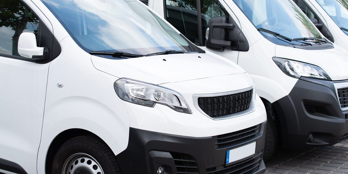 Weiße Nutzfahrzeuge stehen in einer Reihe versetzt nebeneinander. nutzfahrzeuge, transporter, logistik, spedition, transportieren, kleintransporter, weiß, personen, güter, leasing, firma, unternehmen, fahrzeug, nutzen, zuladung, last, überladen, fahrzeugklasse, bus, kleinbus, kauf, mieten, mietfahrzeug, umzug