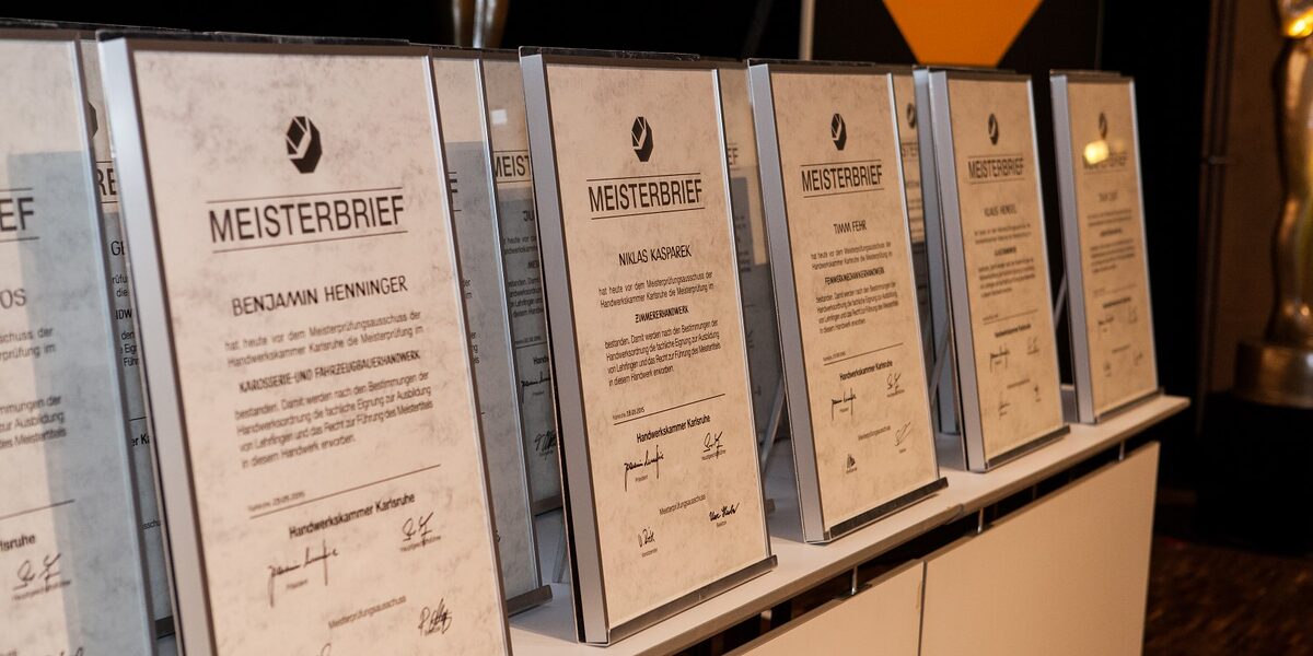 Meisterbriefe stehen eingerahmt auf einem Tisch in einer Reihe. Meisterbriefe