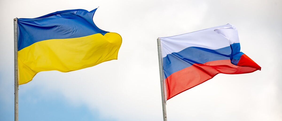 Flagen der Ukraine und Russland. Im Hintergrund blauer Himmel mit Wolken.