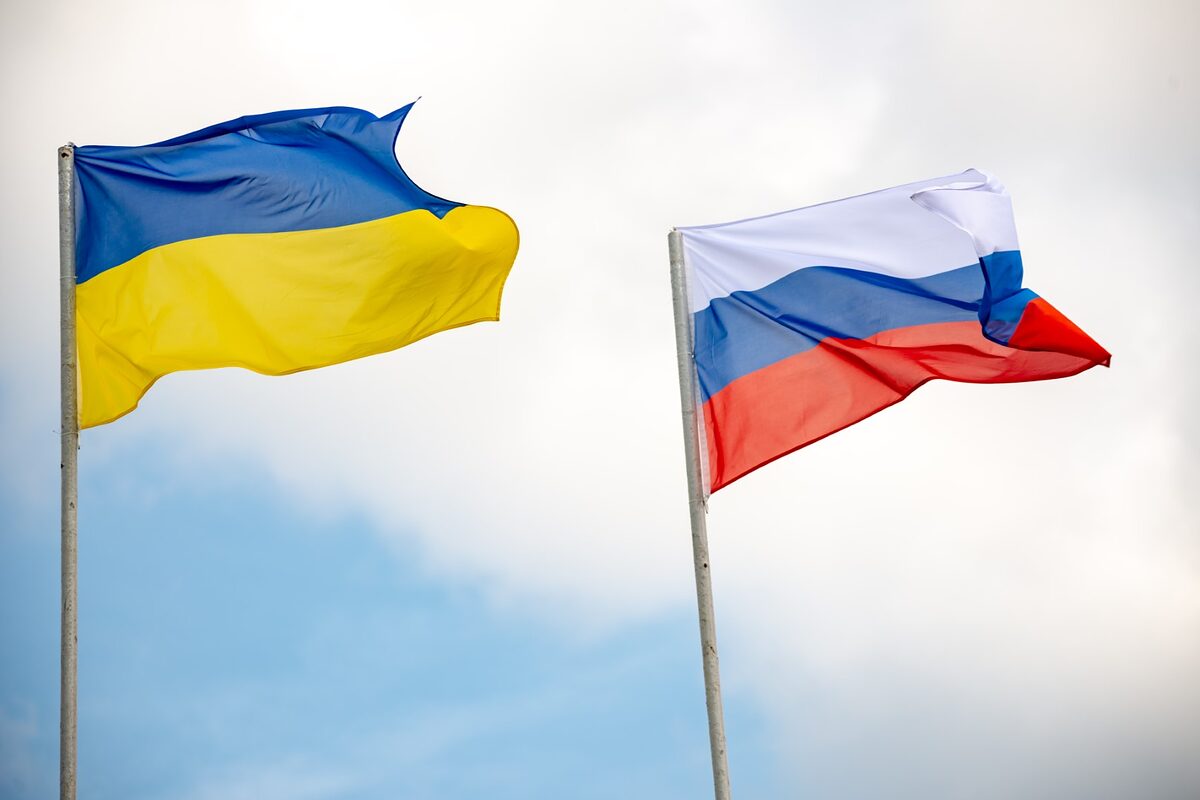 Flagen der Ukraine und Russland. Im Hintergrund blauer Himmel mit Wolken.