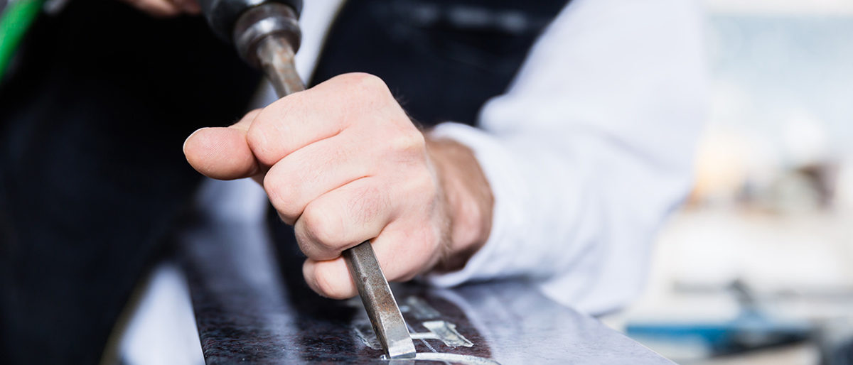 stonemason; man; stone carver; sculptor; stone; craft; handicraft; tombstone; gravestone; headstone; industrial; natural stone; sculpture; carve; cut; treat; handle; men; work; labour; workplace; workshop; handwork; art; artisan; design; style; workpiece; occupation; job; career; tool; chisel; compressed air; Gravure; engraving; inscription; pneumatic; precision; ornament; flourish; indoor; factory; factory hall; building; people; Caucasian; craftsman; handyman; workwear; garb; steinmetz; mann; handwerk; grabstein; industriell; grabmal; hauen; bearbeiten; beruf; bildhauer; stein; naturstein; plastik; skulptur; mnner; arbeit; arbeitsplatz; werkstatt; kunst; kunsthandwerk; gestaltung; handarbeit; werkstck; beschftigung; karriere; anstellung; ausbildung; werkzeug; meiel; druckluft; gravur; inschrift; pressluft; pneumatisch; feinarbeit; przision; verzierung; innen; drinnen; werkhalle; betrieb; menschen; leute; handwerker; arbeiter; arbeitskleidung; handwerkertracht; europisch;
