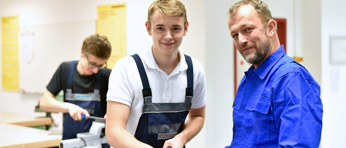 berufsausbildung, azubi, ausbildung, handwerk, industrie, mann, personen, jugendlicher, berufsbildung, auszubildenter, beruf, arbeiten, gruppe, arbeitsplatz, kaukasier, jung, arbeitskleidung, lächeln, fröhlichkeit, lachen, professionell, ausbilden, meister, schüler, lehrling, schule, training, lehren, jugendliche, schraubstock, praxis, praktisch, nachwuchs, karriere, berufsschule, bildung, ausbilder, lehrer, azubis, vor ort, qualifizierung, qualifiziert, tätigkeit, metallbau, stahlbau, werkstück, bauteil, berufsbekleidung, werkstatt, werkstätte, Meister Lehrling ÜLU Überbetriebliche Lehrlingsunterweisung