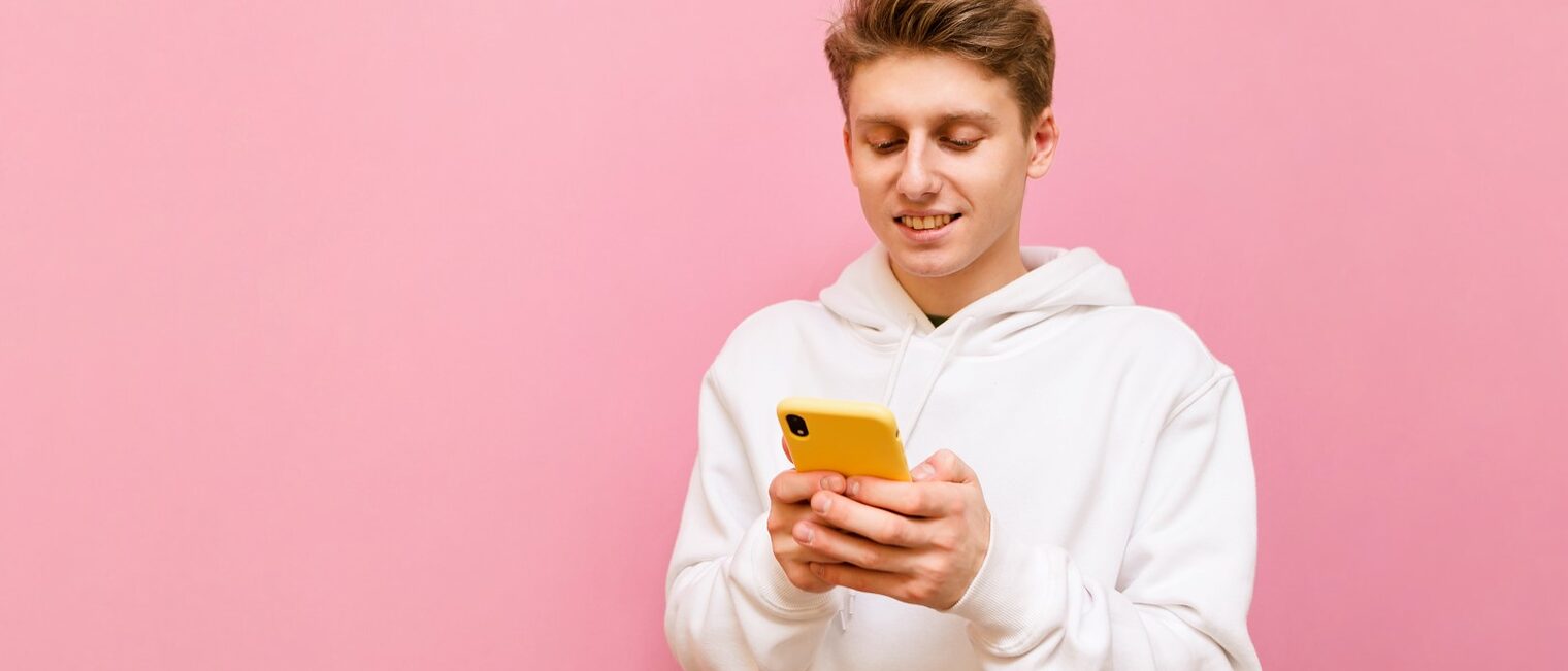 Positive young man standing on a pink background with a smartphone in his hands, looking into the screen and smiling, wearing white casual clothes. Isolated. Copy space Schlagwort(e): phone, smile, mobile phone, modern, message, young, smartphone, text message, enjoy, mobile, cheerful, happy, cyberspace, guy, technology, white, man, joy, male, hand, call, isolated, stylish, pink, handsome, communication, typing, holding, boy, style, happiness, teenage, trendy, schoolkid, portrait, student, background, text, online, read, schoolboy, smart, childhood, person, lifestyle, school, schoolchild, chatting, confident, teenager, phone, smile, mobile phone, modern, message, young, smartphone, text message, enjoy, mobile, cheerful, happy, cyberspace, guy, technology, white, man, joy, male, hand, call, isolated, stylish, pink, handsome, communication, typing, holding, boy, style, happiness, teenage, trendy, schoolkid, portrait, student, background, text, online, read, schoolboy, smart, childhood, person, lifestyle, school, schoolchild, chatting, confident, teenager, Titelbild Digitales Speedating